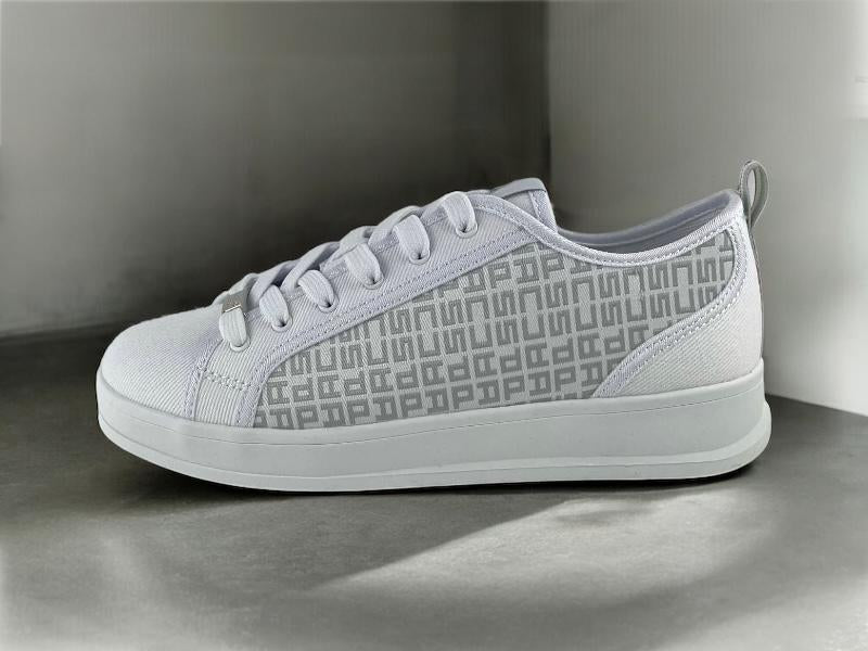 Vista lateral de unos tenis de diseñador, blancos, de mujer, con patrón monograma tipo lujo lateral y cierre de cordones  sobre fondo de cemento. 