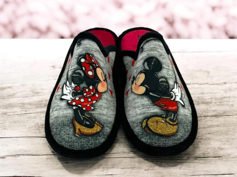 Vista fontal de unas zapatillas descalzas divertidas de Mickey y Minnie sobre fondo de madera blanca.