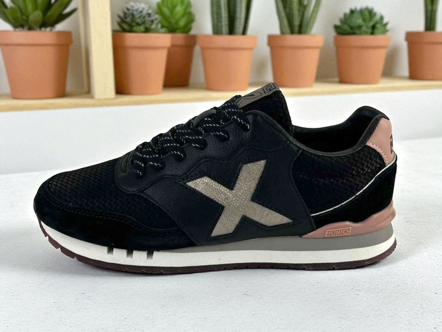 Zapatillas deportivas urbanas, de la marca Munich para mujer, en color negro, logo de la marca metálico X y detalles en el talón en color rosa. Suela antideslizantebicolor blanca y gris.