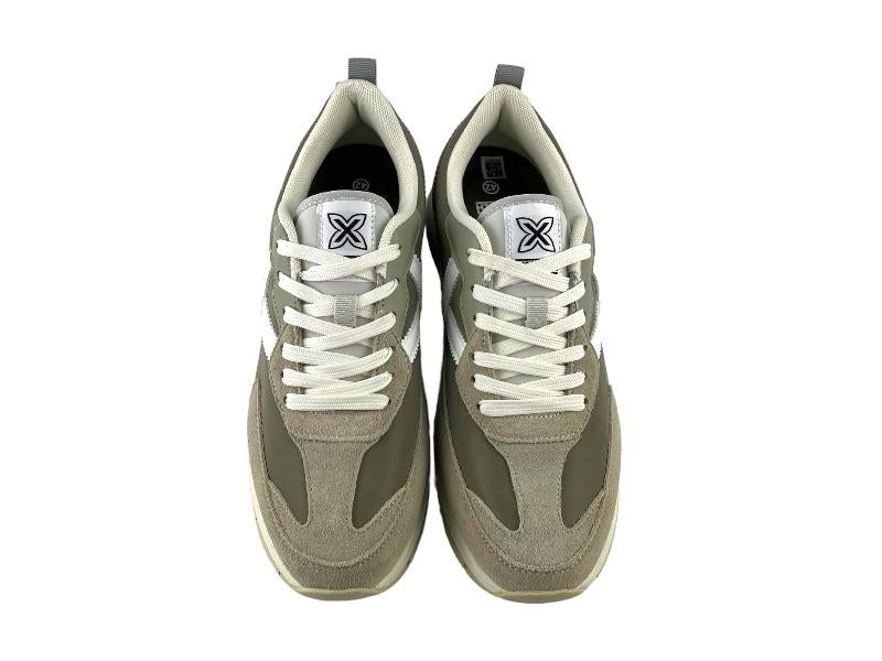 Sneakers ( tenis) de hombre, en tono gris verdoso y logo en la lengüeta de la marca, con cordones y suela en color blanco. Vista frontal sobre fondo blanco.