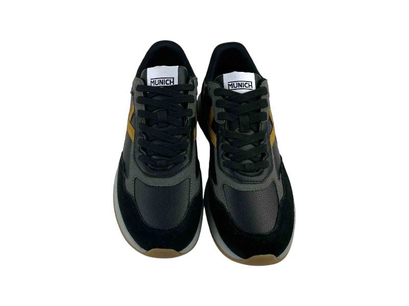 Zapatillas de la marca Munich, en piel color negro, con detalles en ocre y logo de la marca en la solapa, laterales y talonera. Suela en color gris y color caramelo.