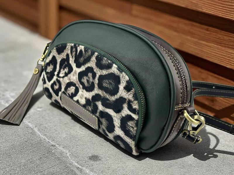 Bolso de mujer de la marca Caramelo, con bolsillos exteriores, en animal print leopardo y piel lisa, marrón chocolate y verde oscuro, con forma redonda y borla a juego.