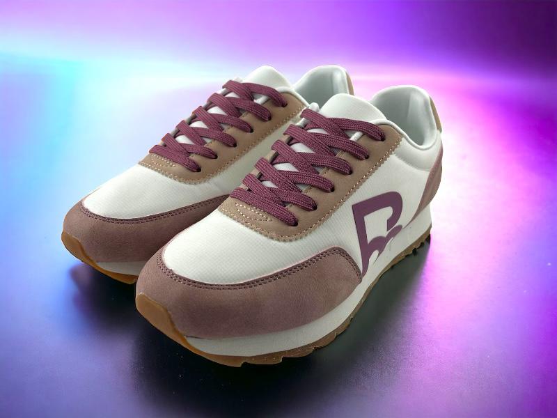 Sneakers de mujer de la marca Pepe Moll, en color blanco con puntera, cordones y logo en color rosa. Vista lateral izquierda sobre fondo luminoso en tonos rosas y azules.