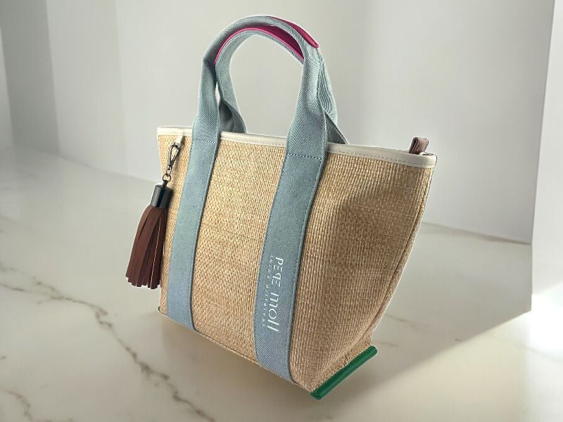 Bolso vegano de mujer en rafia, con detalles en vaquero en asas. Pompón en cuero vegano extraíble. Vista lateral derecha sobre fondo de mármol blanco.