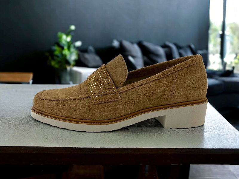 Mocasín de mujer en piel ante beige, con tacón bajo y suela en blanco. Vista lateral izquierda  sobre fondo de madera blanca.