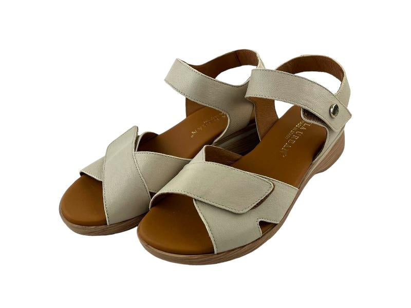 Sandalias planas de mujer con tiras regulables cruzadas en color beige y pulsera en el tobillo. Vista lateral izquierda de las sandalias sobre fondo blanco. 