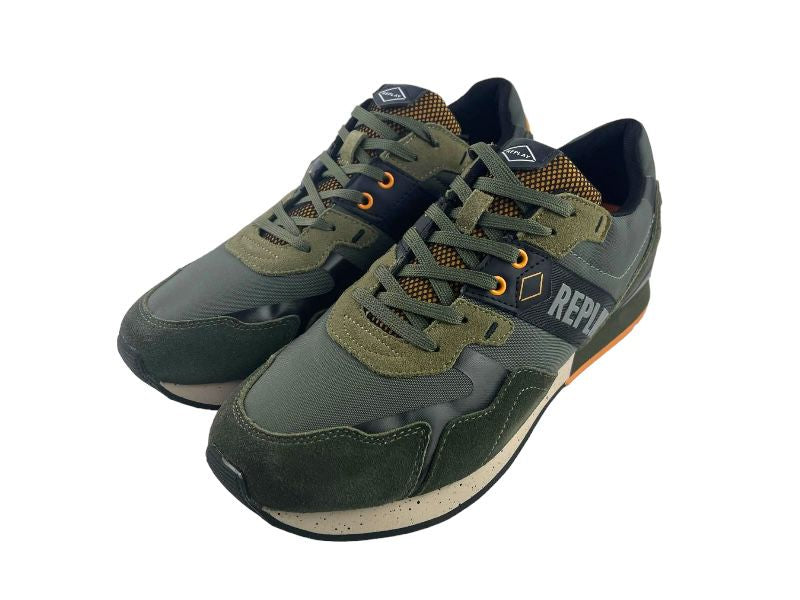 Sneakers de hombre con cordones en color verde y detalles en naranja. Con logo en el lateral  y en la lengüeta de la marca. Vista lateral izquierda de los tenis sobre fondo gris.