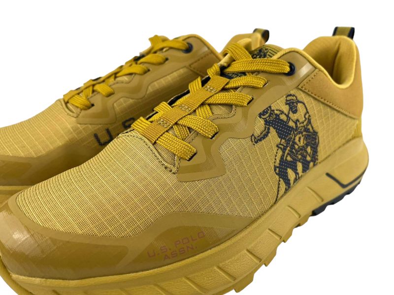 Vista detalle lateral exterior e unos tenis de hombre en color amaillo y logo en azul marino de la marca  U.S.Polo Assn con cordones amarillos.