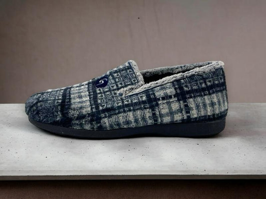Pantuflas cerradas de casa para hombre en paño textil de cuadros, grises y azules, con suela de goma sobre fondo de mármol.