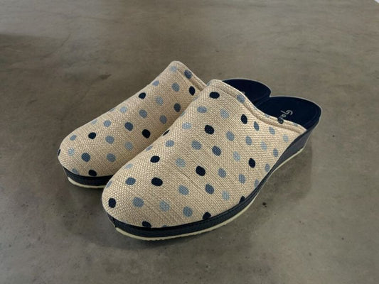 Zapatillas de mujer con topos sobre fondo beige, cuña en color marino. Vista lateral izquierda de las zapatillas sobre fondo metálico beige.