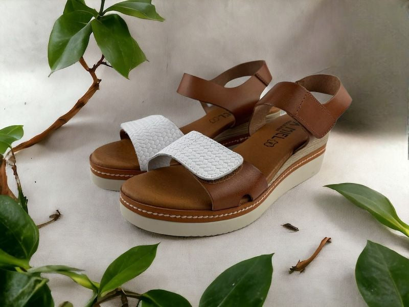 Sandalias de mujer en piel, con cuña, en color cuero y blanco. Vista lateral izquierda sobre fondo floral.