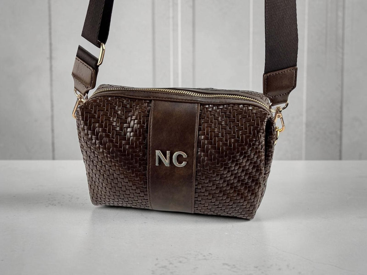 Bandolera Noco marrón chocolate de piel vegana trenzada, detalle NC, correa regulable y herrajes dorados, vista frontal.
