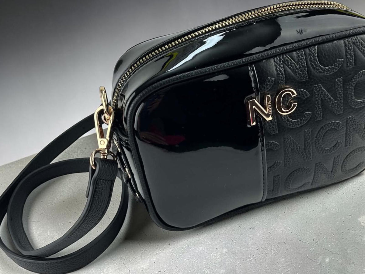 Bandolera Noco negra de piel vegana con textura NC en relieve, acabado brillante, correa regulable y herrajes dorados, vista lateral.