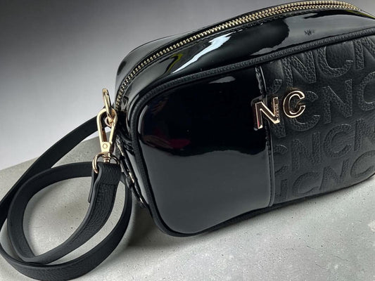 Bandolera Noco negra de piel vegana con textura NC en relieve, acabado brillante, correa regulable y herrajes dorados, vista lateral.