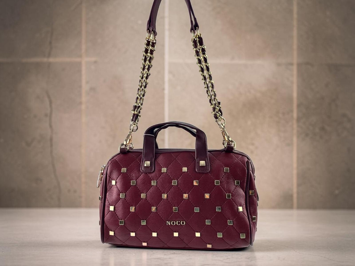 Bolso bowling Noco granate de piel vegana con tachas metálicas, asas cortas y cadena dorada, vista frontal.