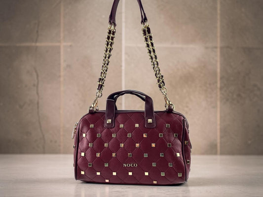Bolso bowling Noco granate de piel vegana con tachas metálicas, asas cortas y cadena dorada, vista frontal.