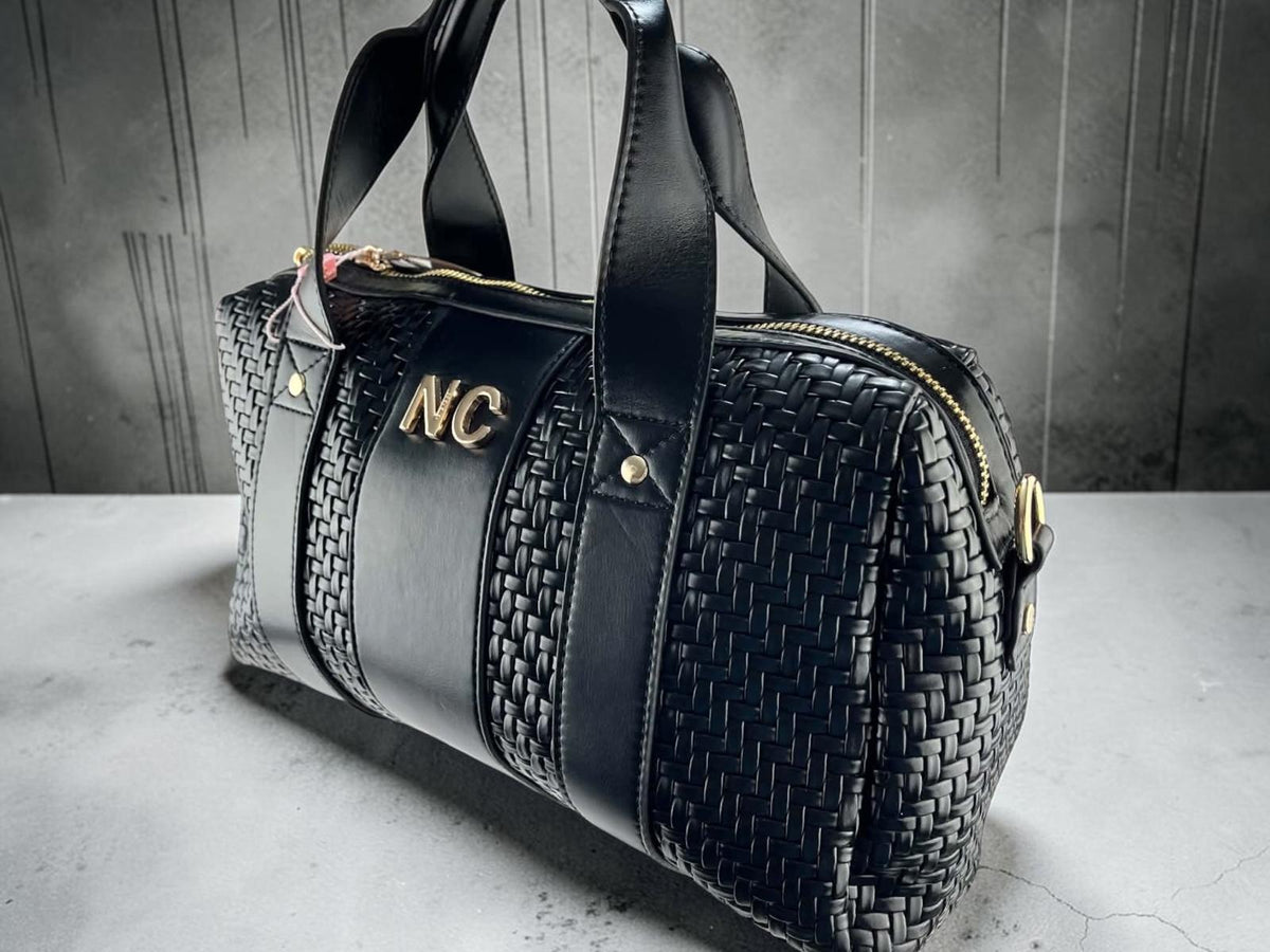 Bolso bowling Noco negro de piel vegana con laterales trenzados, asas cortas, detalle NC y herrajes dorados, vista frontal.
