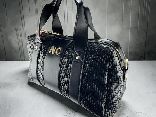 Bolso bowling Noco negro de piel vegana con laterales trenzados, asas cortas, detalle NC y herrajes dorados, vista frontal.
