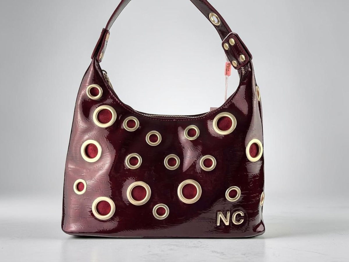 Bolso góndola Noco burdeos de piel vegana efecto charol con ojales metálicos dorados y detalle NC, vista frontal.