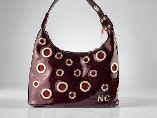 Bolso góndola Noco burdeos de piel vegana efecto charol con ojales metálicos dorados y detalle NC, vista frontal.