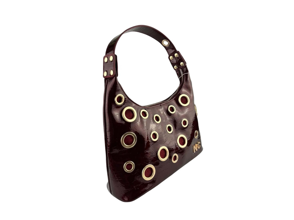 Vista lateral del bolso góndola Noco burdeos de piel vegana charol con ojales dorados, textura brillante y asa regulable.