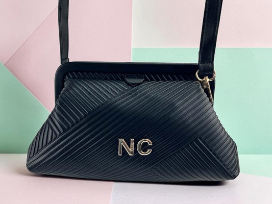 Bolso de mano Noco negro de piel vegana con textura plisada diagonal, detalle NC y correa extraible, vista frontal.