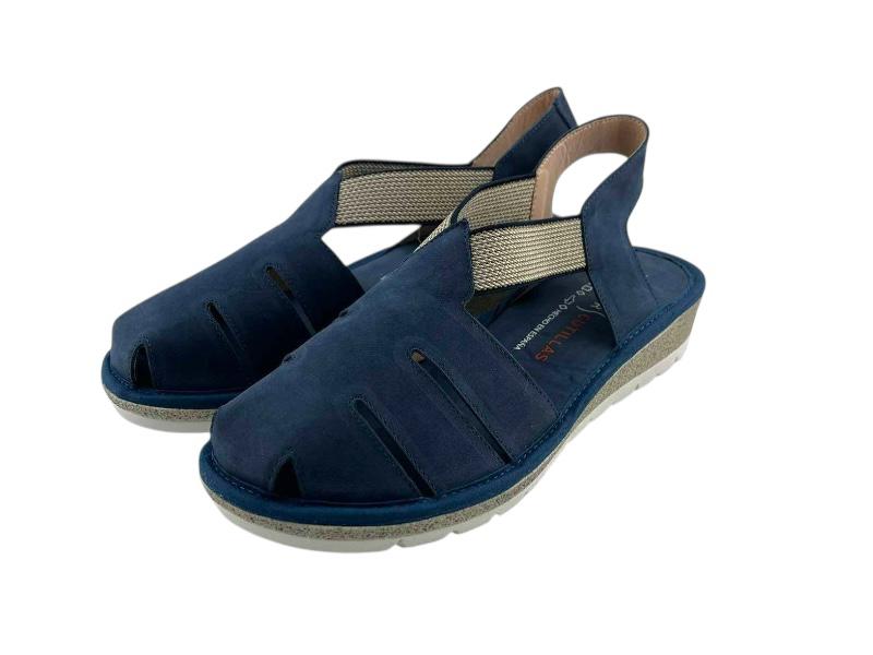 Vista lateral izquierda de unas sandalias planas en piel azul, de cortes asimétricos, con elásticos en el empeine y puntera cerrada sobre fondo blanco.