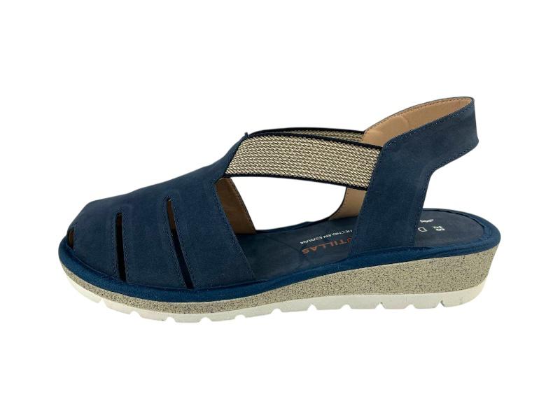 Vista lateral izquierda de unas sandalias planas en piel azul, de cortes asimétricos, con elásticos en el empeine, suela blanca de goma y puntera cerrada sobre fondo blanco..