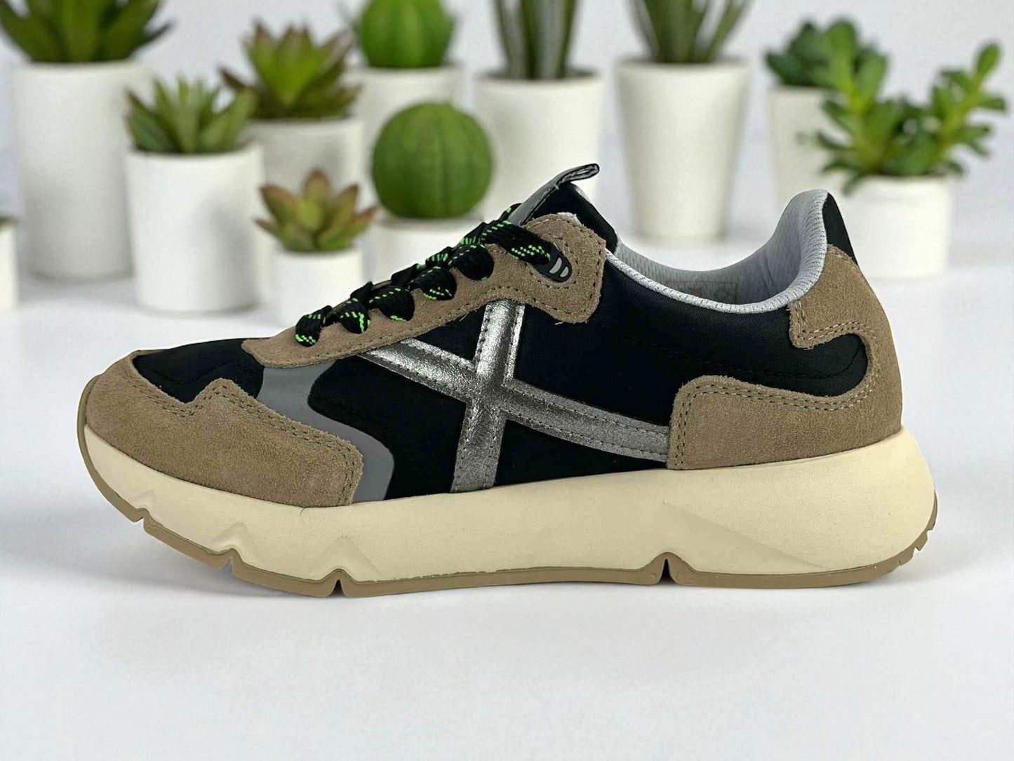 Zapatilla deportiva de moda unisex de la marca Munich con detalles en plata y beige sobre fondo negro.