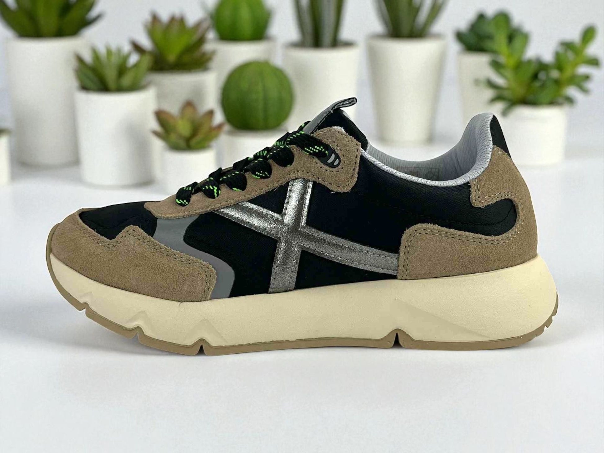 Zapatilla deportiva de moda unisex de la marca Munich con detalles en plata y beige sobre fondo negro.