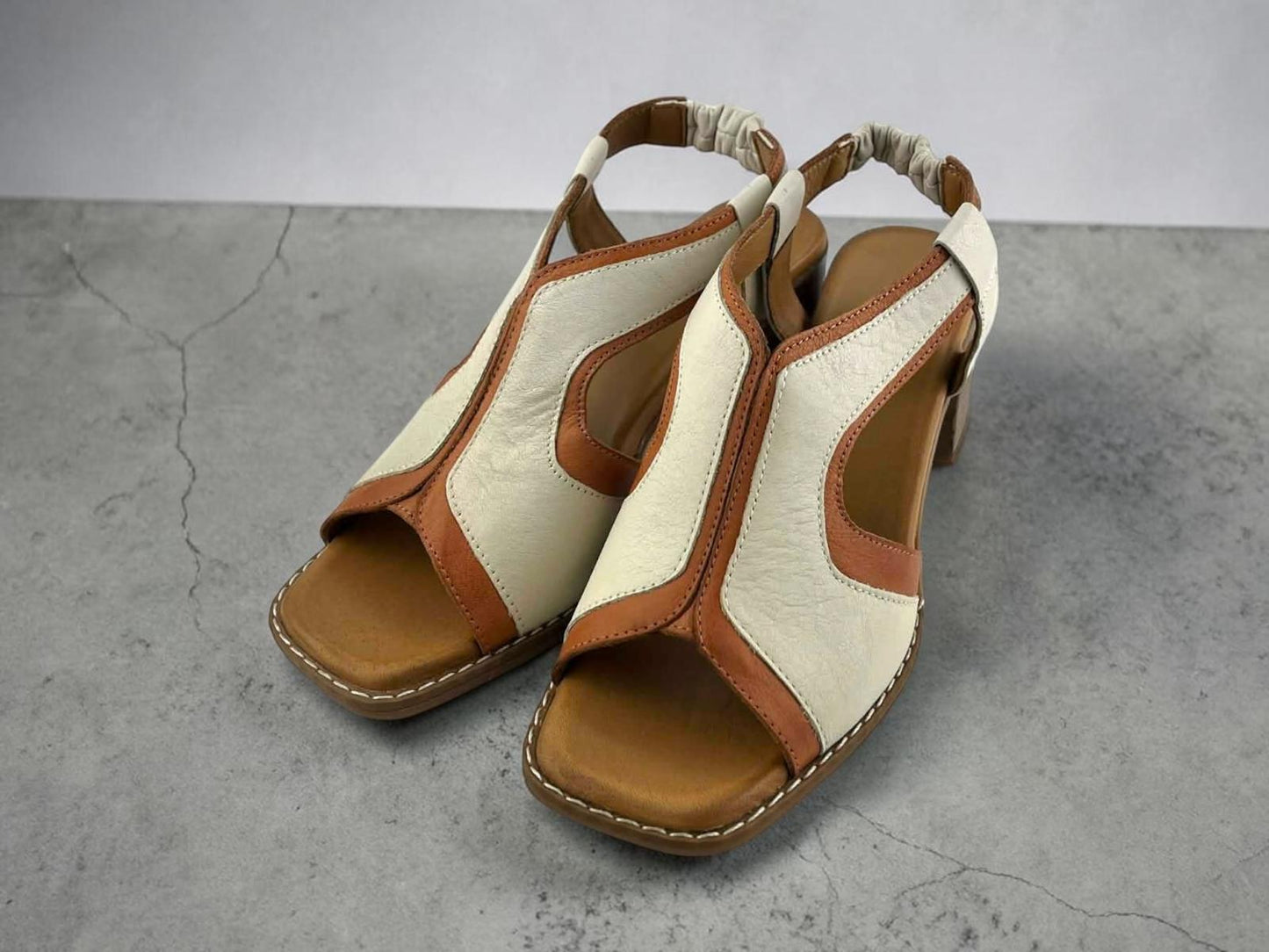 Sandalias de piel bicolor en blanco y marrón con diseño de cortes geométricos y tacón bloque estable de media altura.
