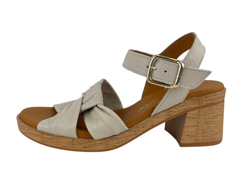 Vista lateral izquierda de unas sandalias de moda en cuero beige, con tacón medio, plataforma y cierre de hebilla al tobillo, presentadas sobre un fondo blanco.