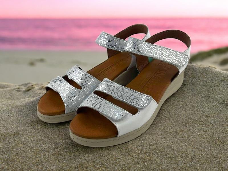 Sandalias blancas ergonómicas de mujer, con cuña, en piel, con cierre de velcro regulable  en empeine y pala, con detalles de piel en color plata y  plantilla acolchada color caramelo muy cómoda.
