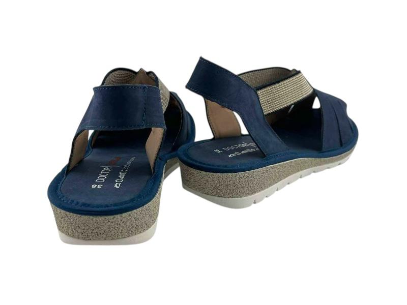 Vista por la parte de atrás de unas sandalias planas, en color azul, abiertas por la parte de atrás y puntera cerrada sobre fondo blanco.