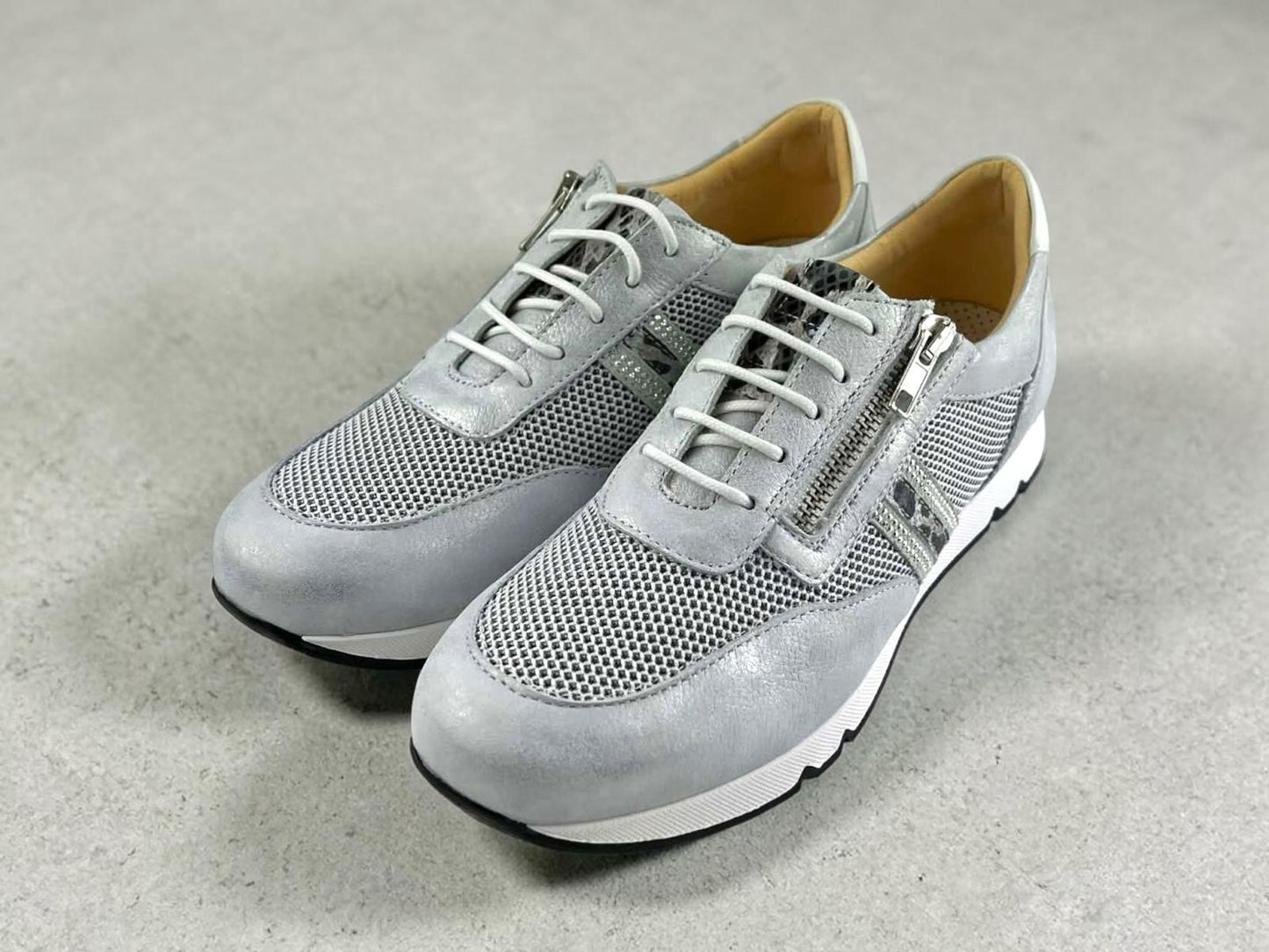 Sneakers plateadas para mujer con paneles de rejilla, cordones blancos y cremallera lateral metálica sobre suela blanca.