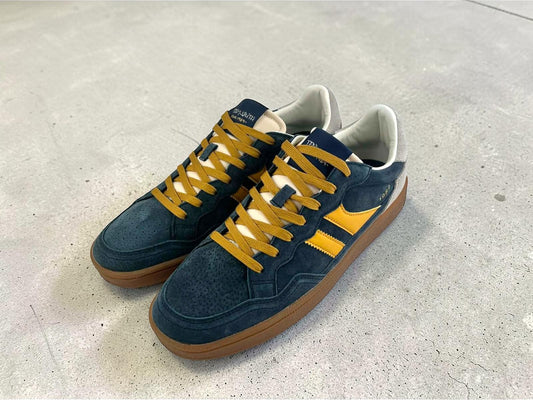 Vista diagonal donde se aprecia el diseño completo del par de sneakers para hombre Teddy Smith, con combinación azul marino y amarillo, los cordones de contraste y la suela caramelo.
