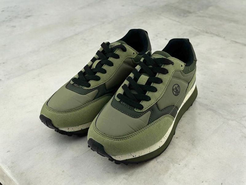 Tenis deportivos de mujer de la marca Pepe Moll, con diseño moderno en tonos verdes y negros, suela negra antideslizante, y logo lateral distintivo. Están colocados sobre una superficie clara, ideales con cualquier look urbano.