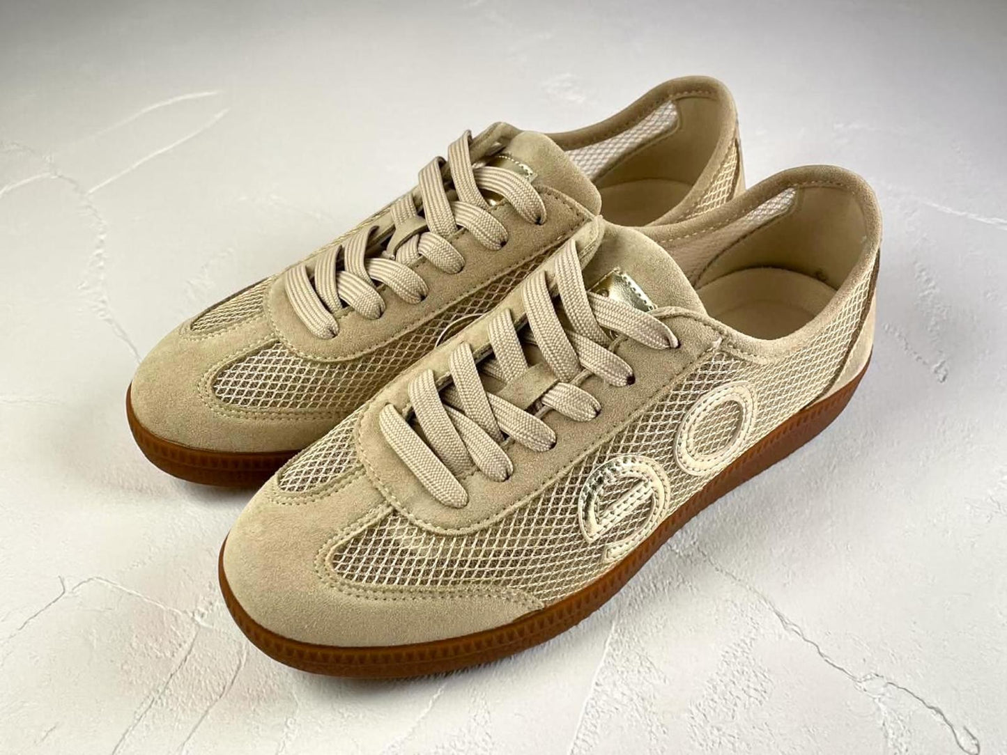 Zapatillas deportivas en color beige con paneles de rejilla calada, detalles de ante y suela de goma color caramelo.