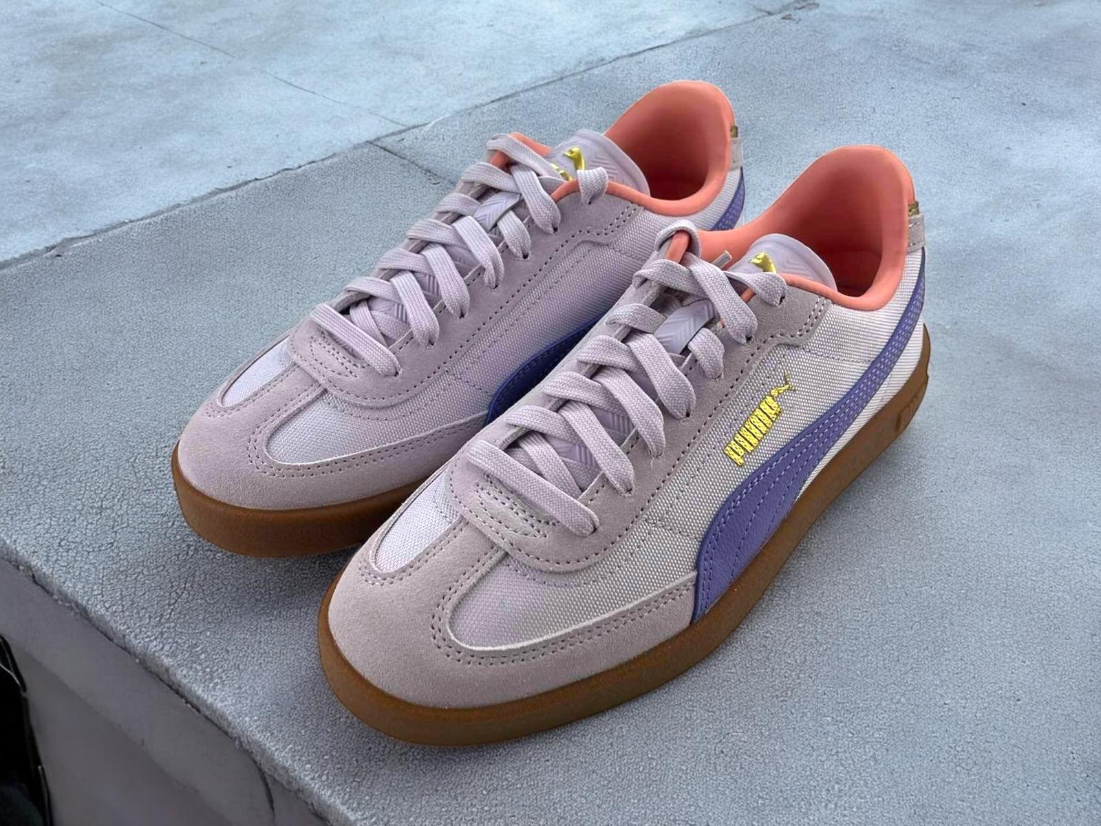 Zapatillas para mujer Puma clásicas, color lila con franja violeta, detalles dorados de la marca y suela de goma marrón.
